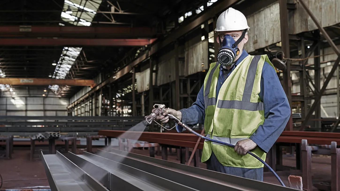 Worker spraying a protective coating on steel