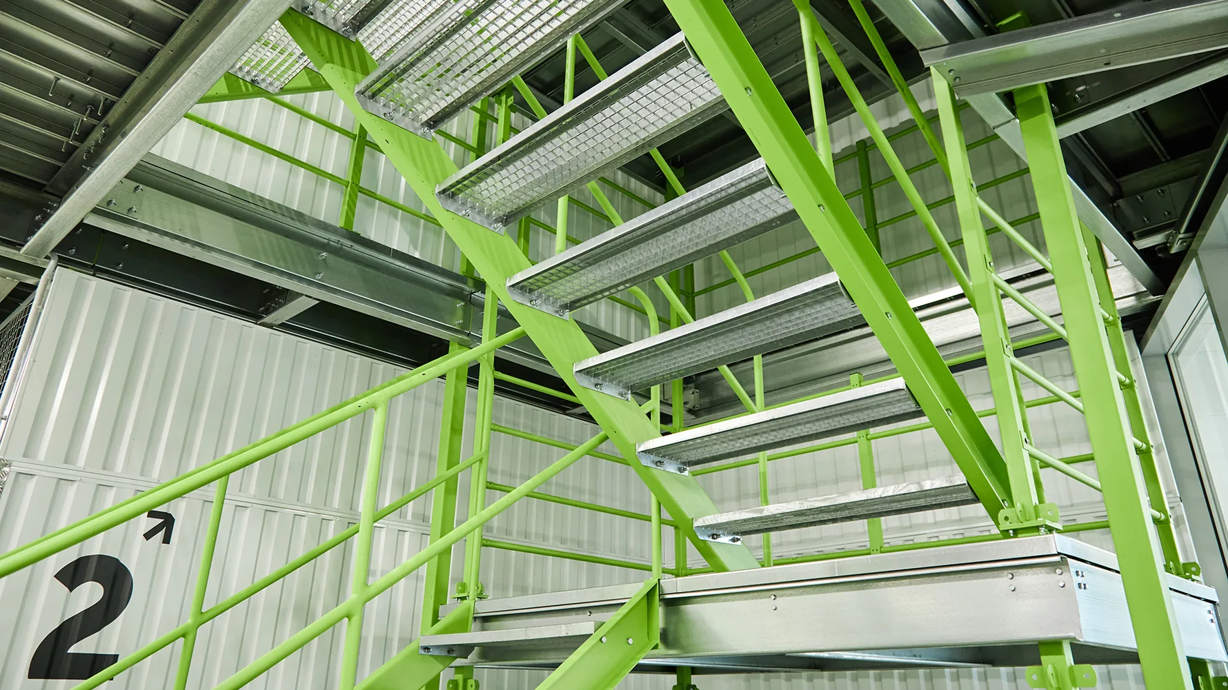 Bright green internal industrial access staircase with open steel treads and handrails