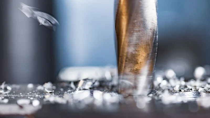 Close-up of a drill bit cutting into steel, with metal swarf around it